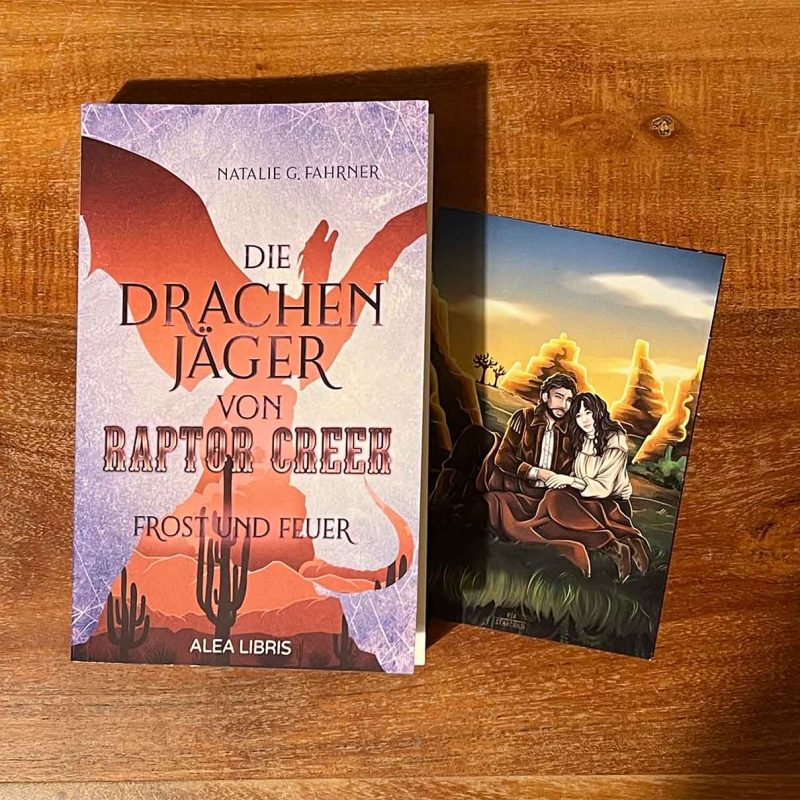 Das Bild zeigt das Buch "Die Drachenjäger von Raptor Creek" und eine Charakterkarte, auf der ein Paar in einer Canyon-Landschaft zu sehen ist.